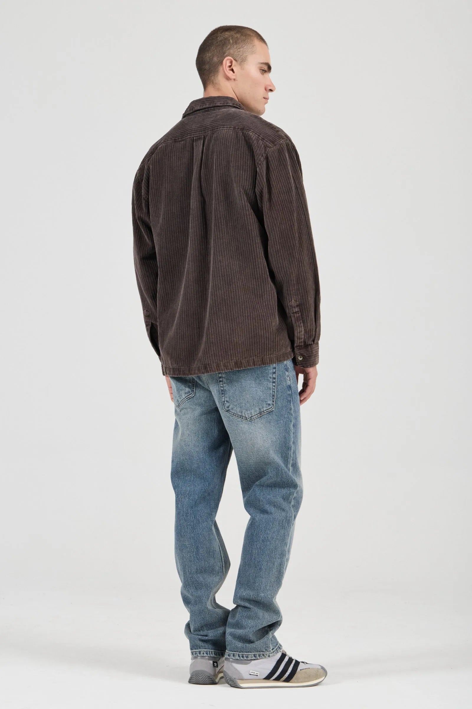 Man wearing a brown shirt and blue jeans on a white background