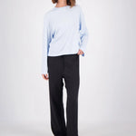 A woman modeling a light blue long-sleeve crewneck top and black wide-leg pants against a plain light gray studio background.