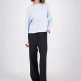 A woman modeling a light blue long-sleeve crewneck top and black wide-leg pants against a plain light gray studio background.