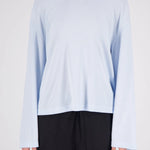 A model wearing a light blue long-sleeve crewneck top and black pants, shown from the neck down against a plain light gray background.