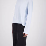 A model wearing a light blue long-sleeve knit top and black wide-leg trousers, shown from the side against a light gray studio background.