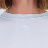 Close-up of a person wearing a light-colored crewneck top, showing the neck, chin, and hair against a plain light background.