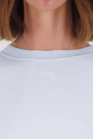 Close-up of a person wearing a light-colored crewneck top, showing the neck, chin, and hair against a plain light background.