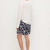 A man shown from the back wearing a white long-sleeve shirt and navy shorts with a white chain-link pattern, paired with black flip-flop sandals, against a plain white studio background.