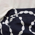 Close-up of a garment waist area showing a navy fabric with a large white chain-link pattern and a white drawstring, paired with a white top.