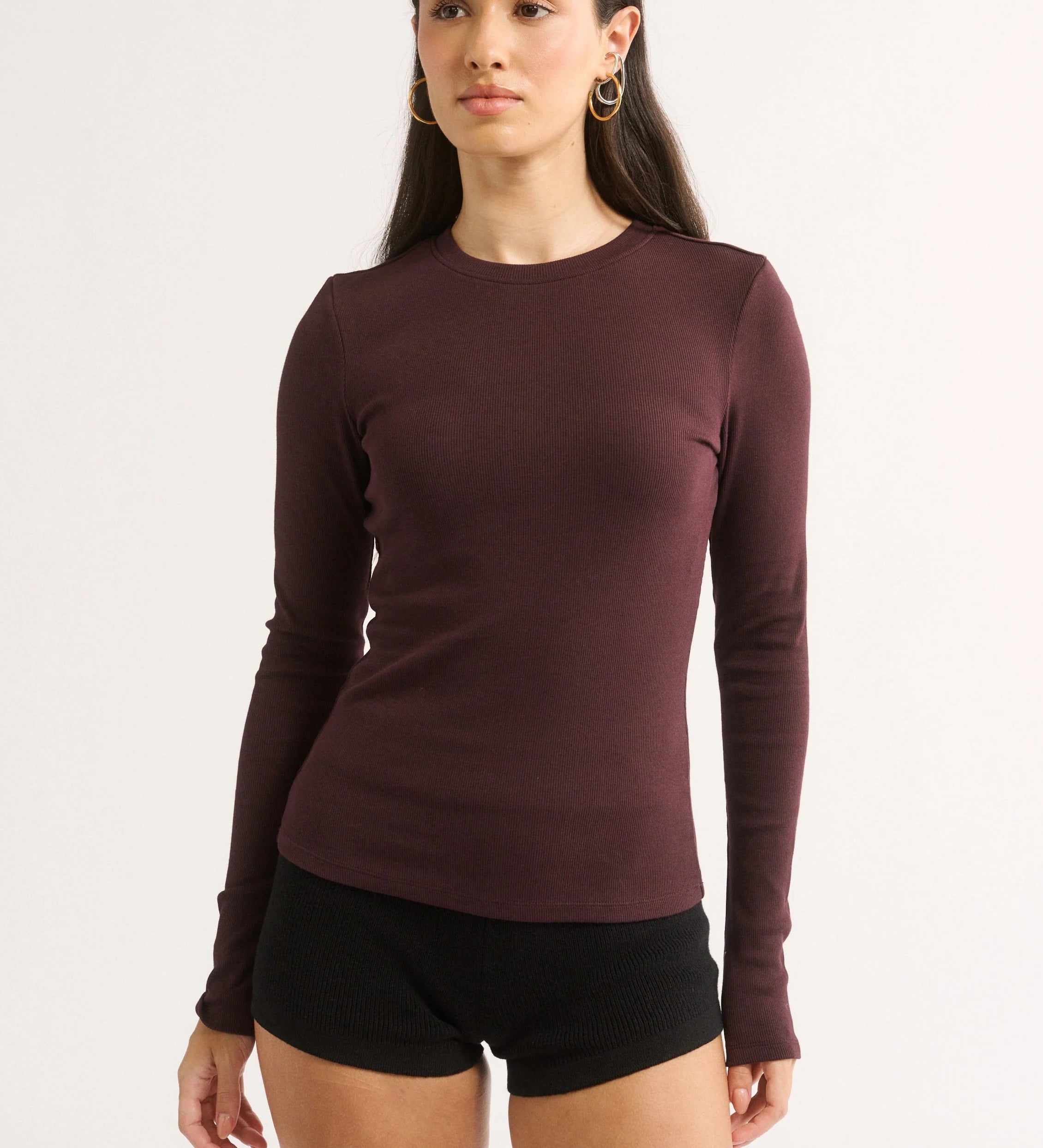Woman wearing a maroon long-sleeve top and black shorts on a white background
