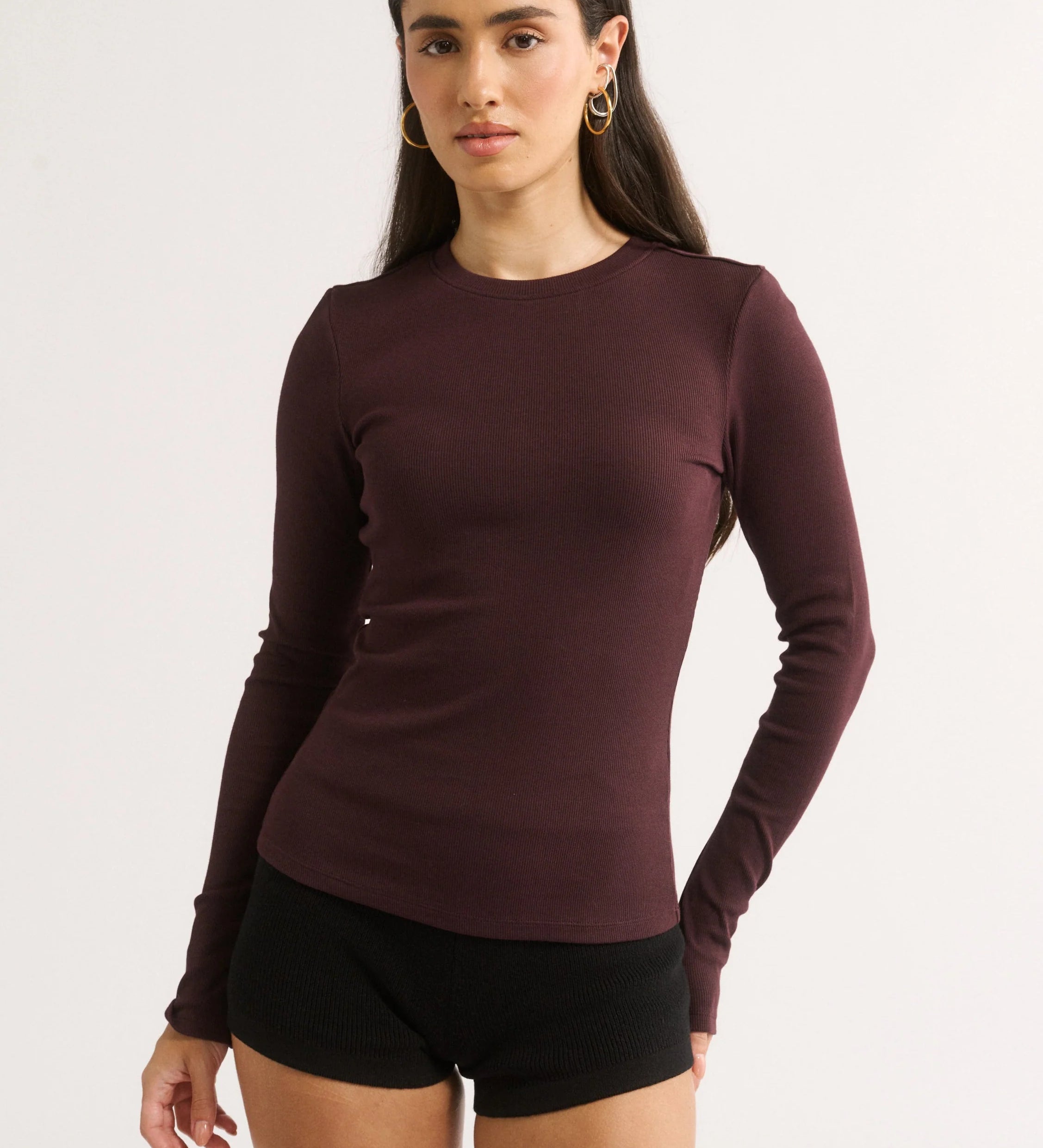 Woman wearing a maroon long-sleeve top and black shorts on a white background