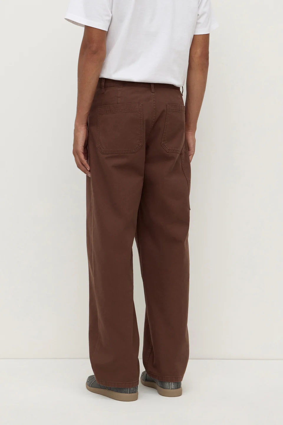 Person wearing brown pants and a white shirt on a white background