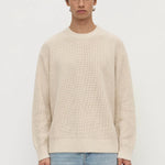 Man wearing a beige sweater and light blue jeans on a white background