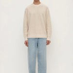 Man wearing a beige sweater and light blue jeans on a white background