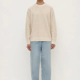 Man wearing a beige sweater and light blue jeans on a white background