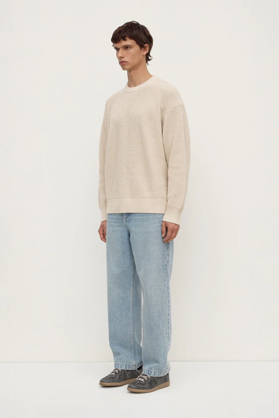 Man wearing a beige sweater and light blue jeans on a white background