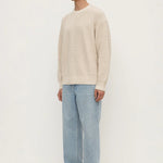 Man wearing a beige sweater and light blue jeans on a white background