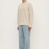 Man wearing a beige sweater and light blue jeans on a white background