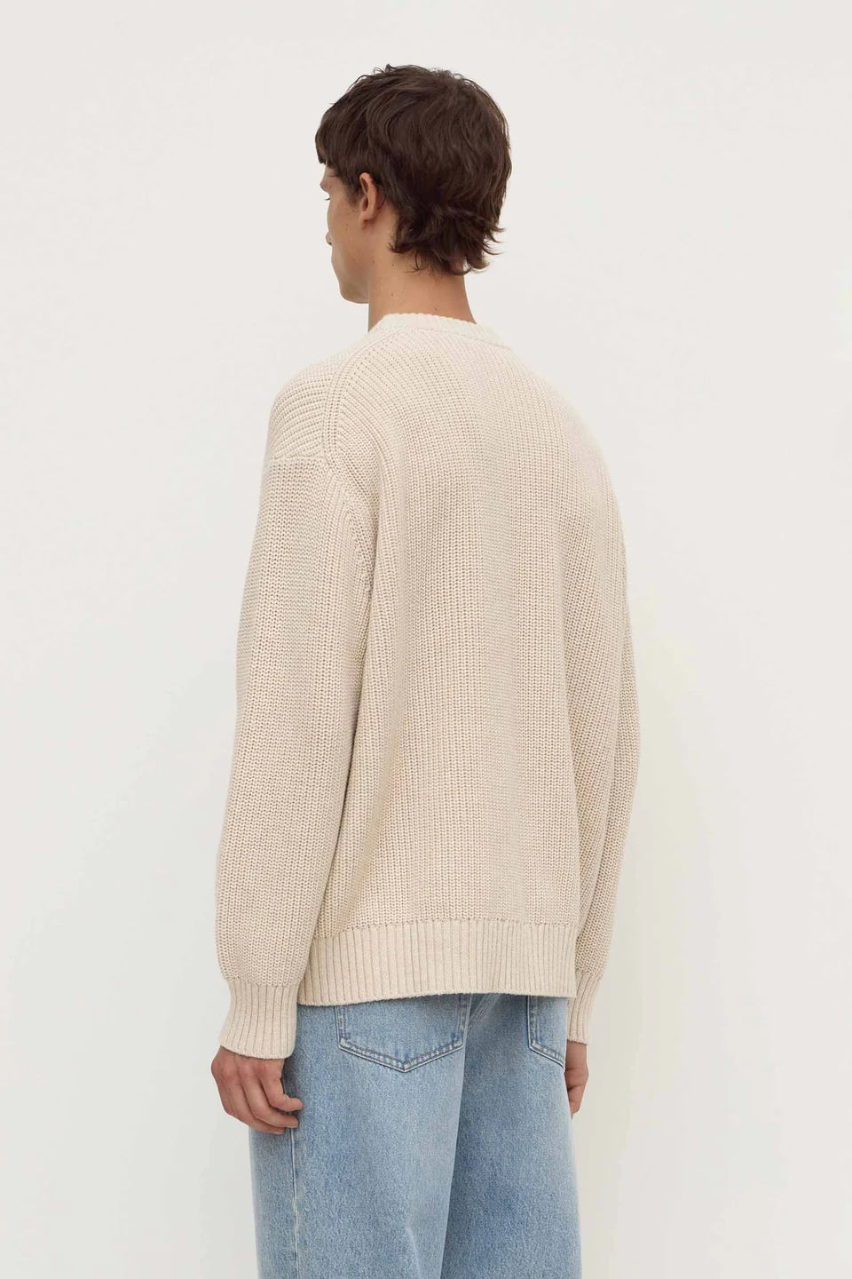 Person wearing a beige sweater and blue jeans on a white background