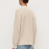 Person wearing a beige sweater and blue jeans on a white background