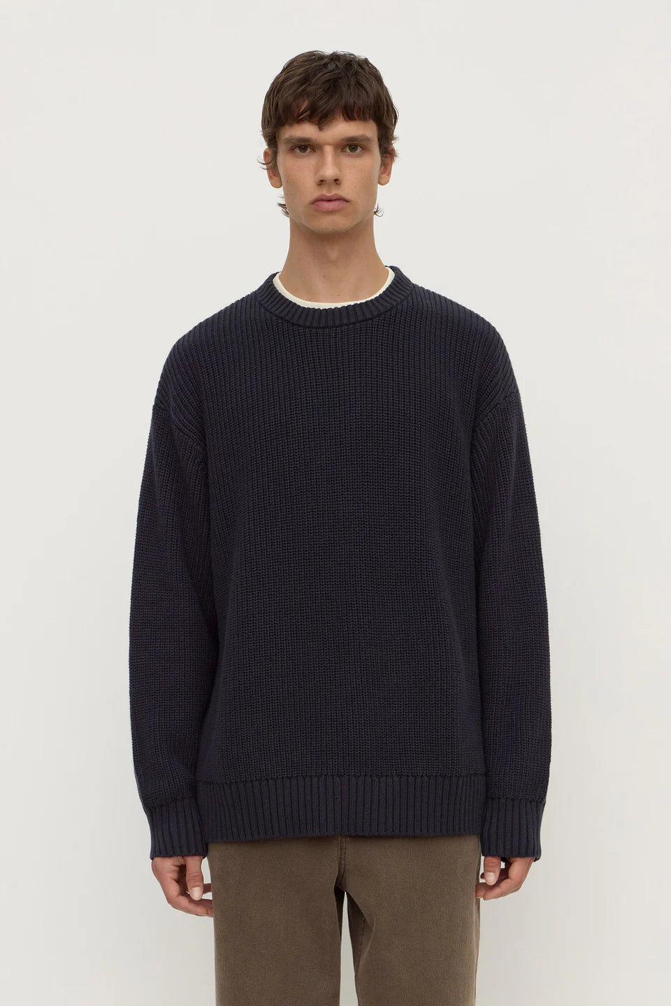 Man wearing a dark blue sweater and brown pants on a white background