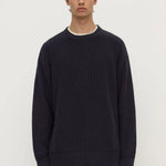 Man wearing a dark blue sweater and brown pants on a white background