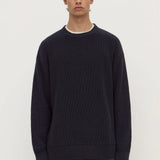 Man wearing a dark blue sweater and brown pants on a white background