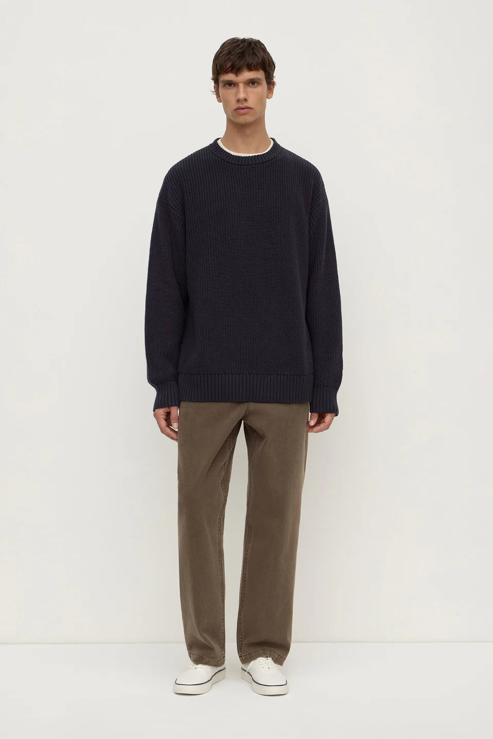 Man wearing a navy sweater and brown pants on a white background