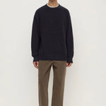 Man wearing a navy sweater and brown pants on a white background