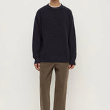 Man wearing a navy sweater and brown pants on a white background