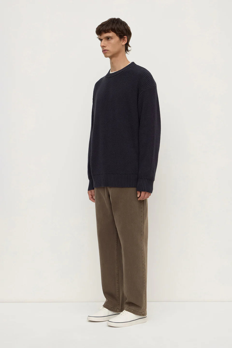 Man wearing a navy sweater and brown pants on a white background