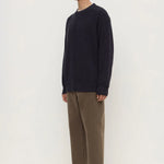 Man wearing a navy sweater and brown pants on a white background