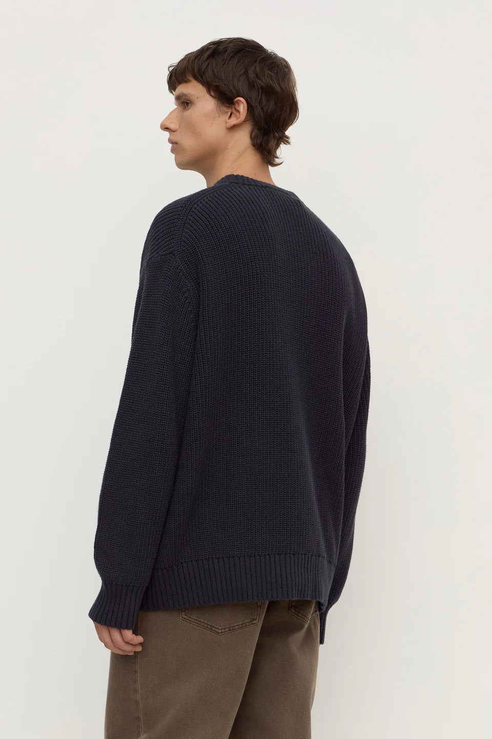 Person wearing a dark blue sweater and brown pants on a white background
