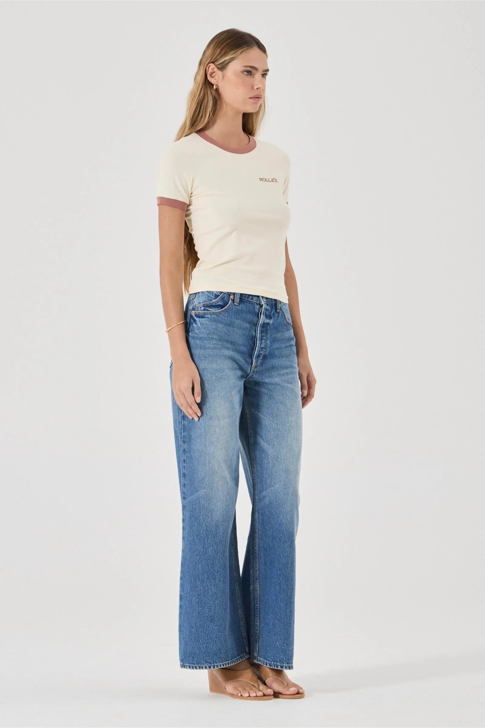 Woman wearing a cream t-shirt and blue jeans on a white background