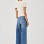 Woman wearing a cream top and blue jeans on a white background