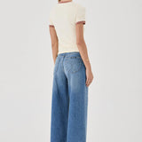Woman wearing a cream top and blue jeans on a white background
