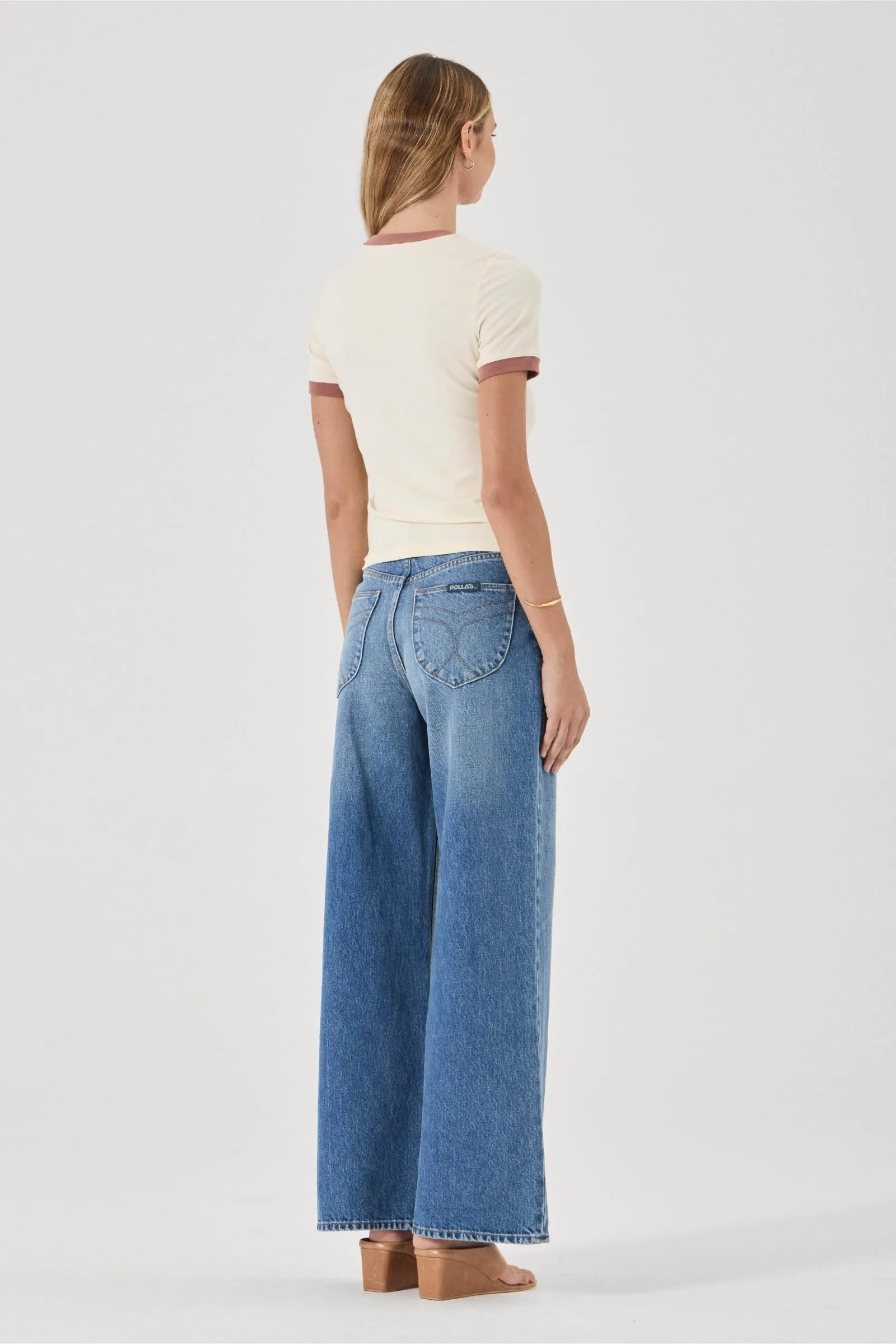 Woman wearing a cream top and blue jeans on a white background