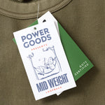 Green sweatshirt with Power Goods label and tag on a green surface