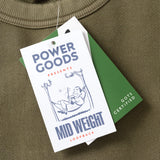 Green sweatshirt with Power Goods label and tag on a green surface