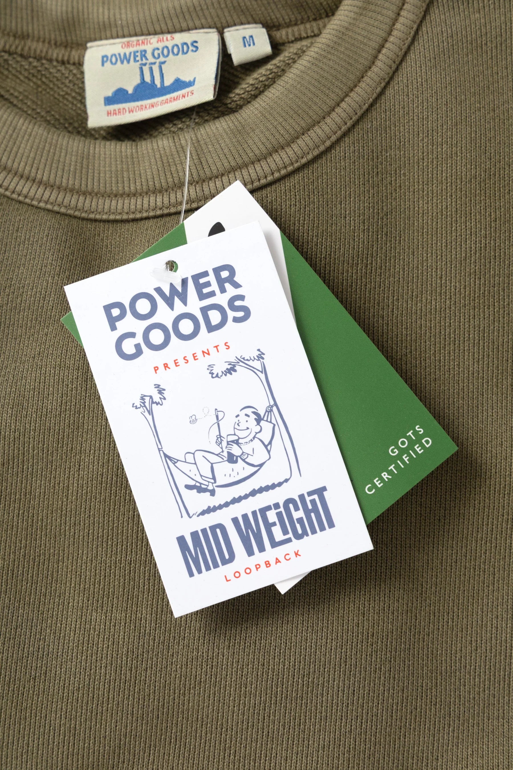 Green sweatshirt with Power Goods label and tag on a green surface