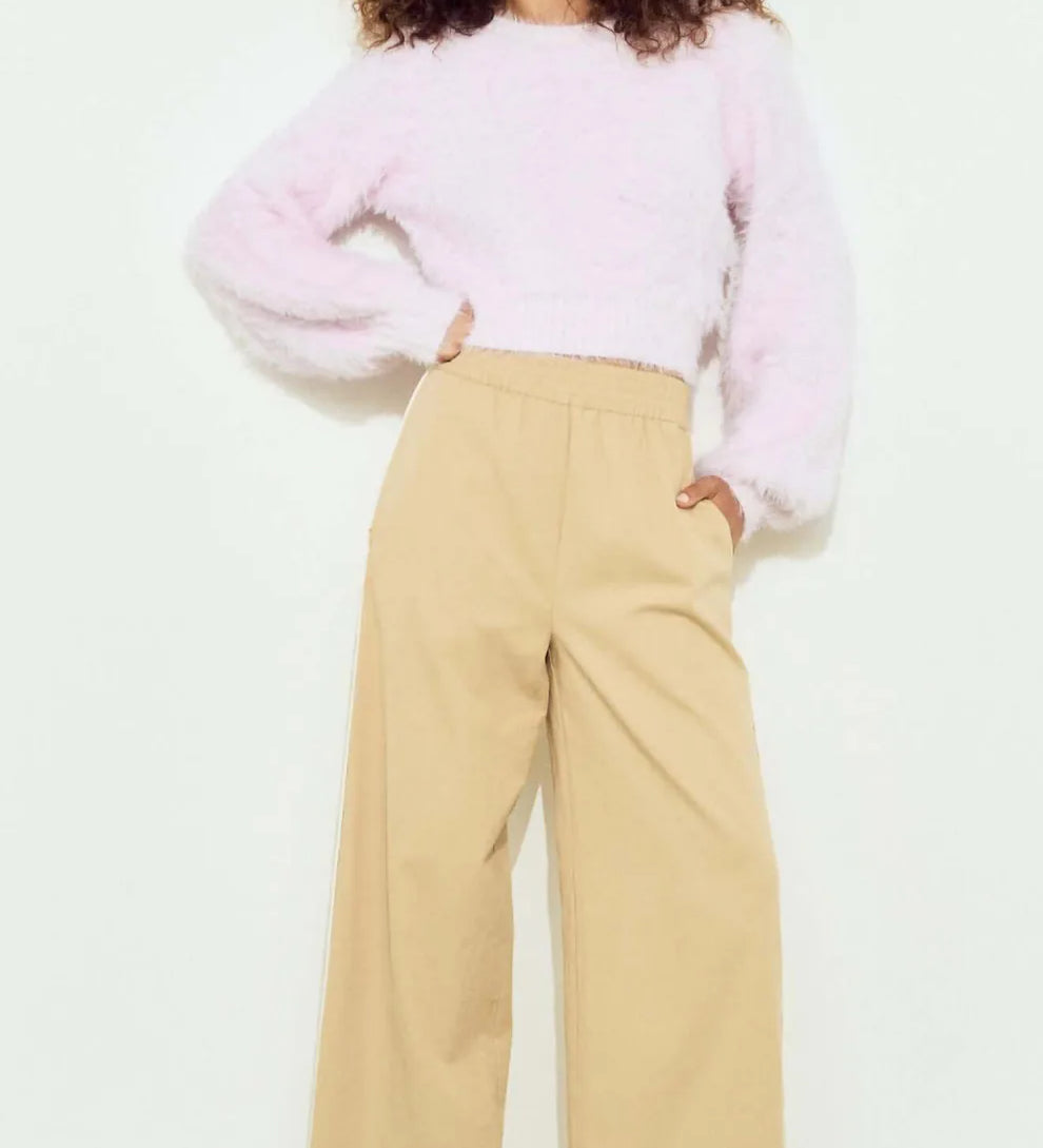 Woman wearing a light pink sweater and beige pants on a white background