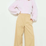 Woman wearing a light pink sweater and beige pants on a white background