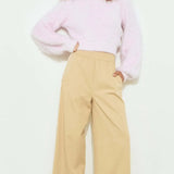 Woman wearing a light pink sweater and beige pants on a white background