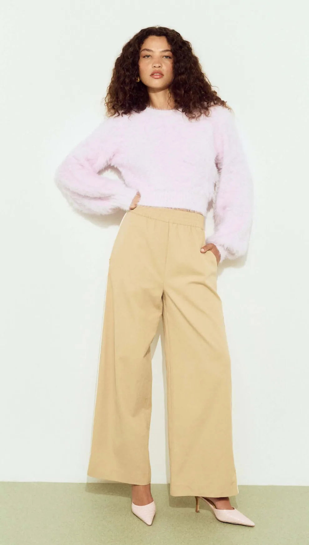 Woman wearing a light pink sweater and beige pants on a white background