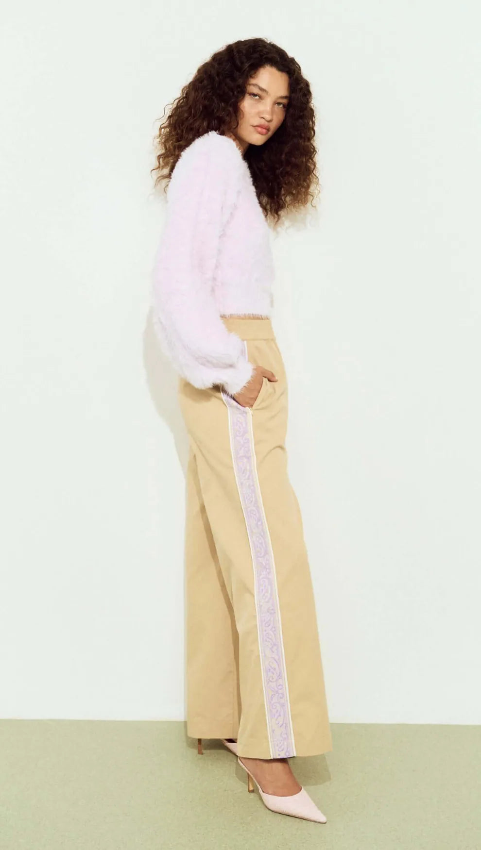 Woman wearing a light pink top and beige pants with a white background