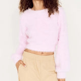 Woman wearing a light pink sweater and beige pants against a white background