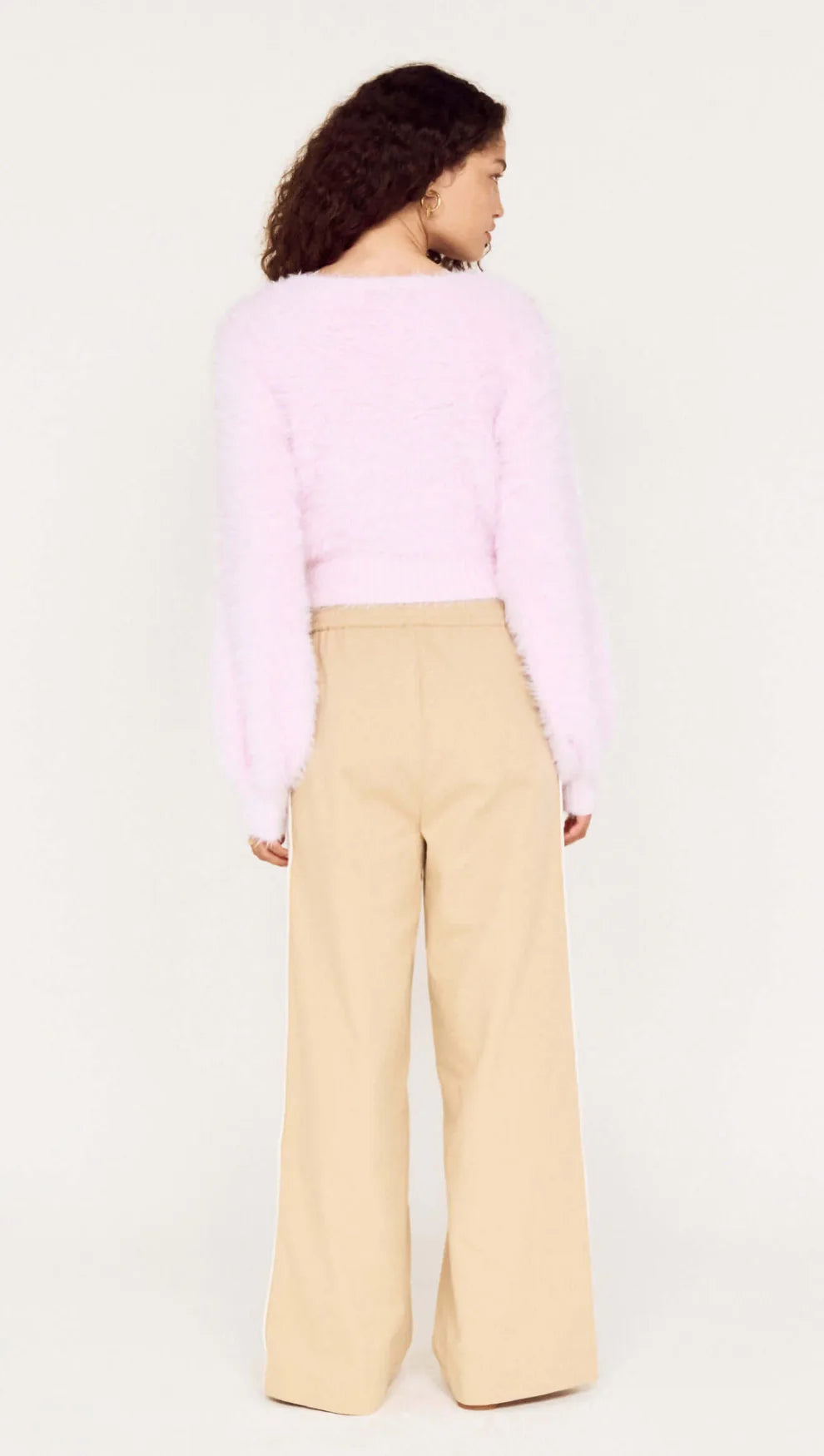 Person wearing a pink sweater and beige pants on a white background