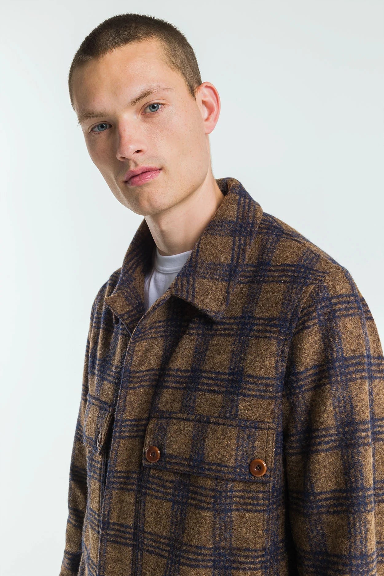 Man wearing a brown and blue plaid coat against a white background
