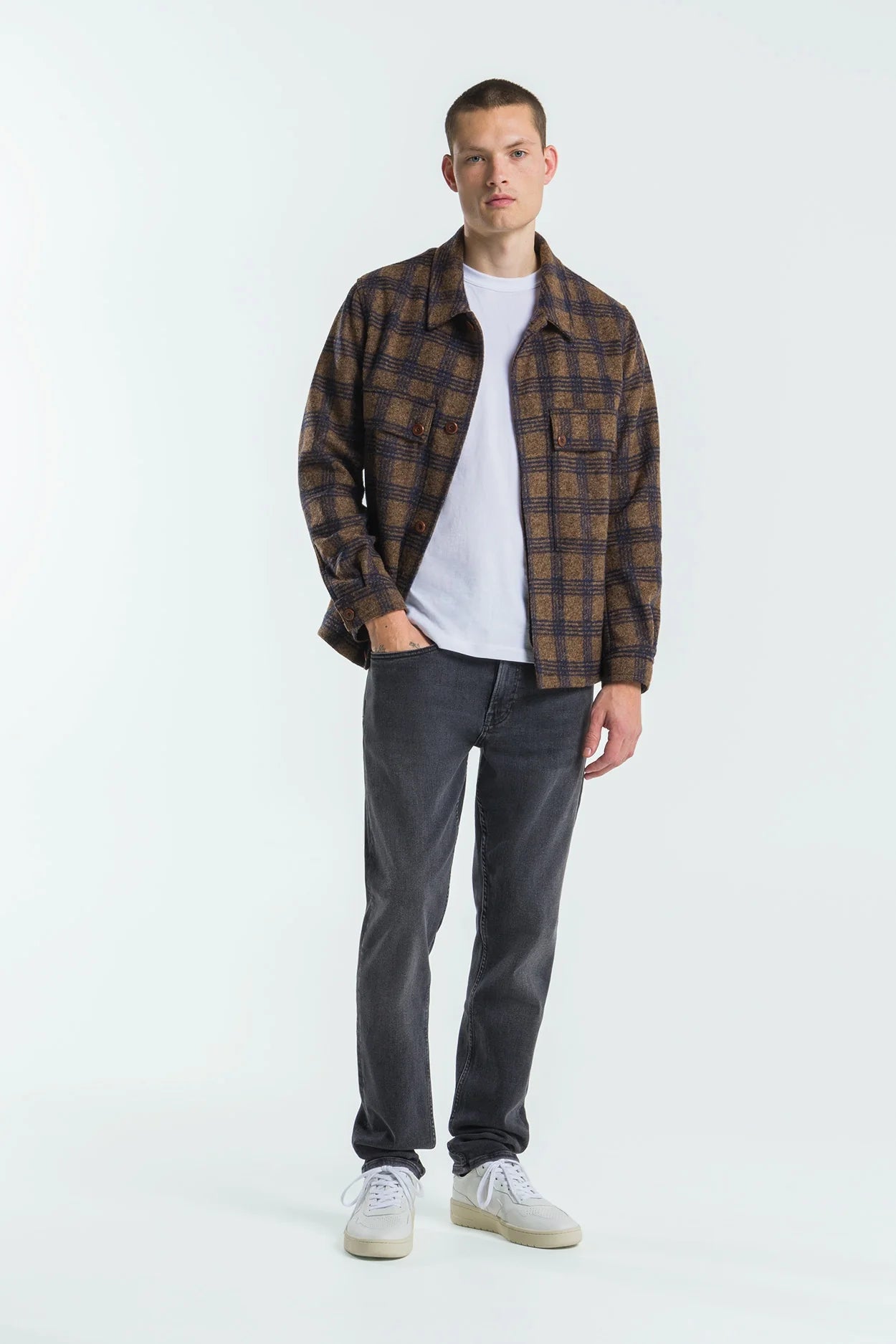 Man wearing a plaid shirt, white t-shirt, gray jeans, and white sneakers on a white background