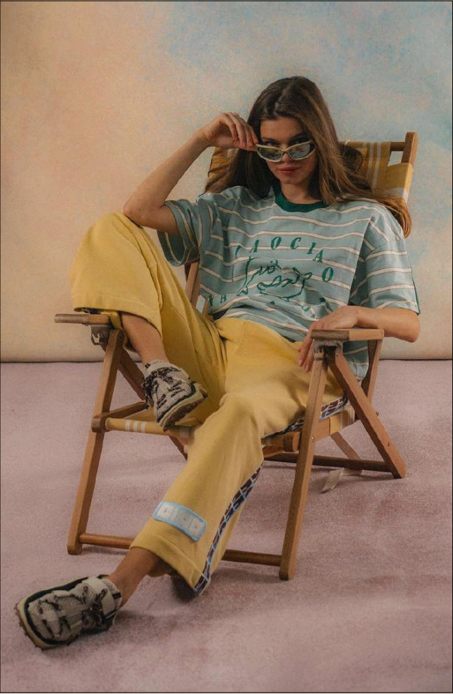 Person sitting on a chair wearing a striped shirt and yellow pants in a casual setting.