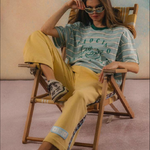 Person sitting on a chair wearing a striped shirt and yellow pants in a casual setting.