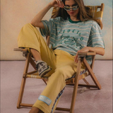 Person sitting on a chair wearing a striped shirt and yellow pants in a casual setting.