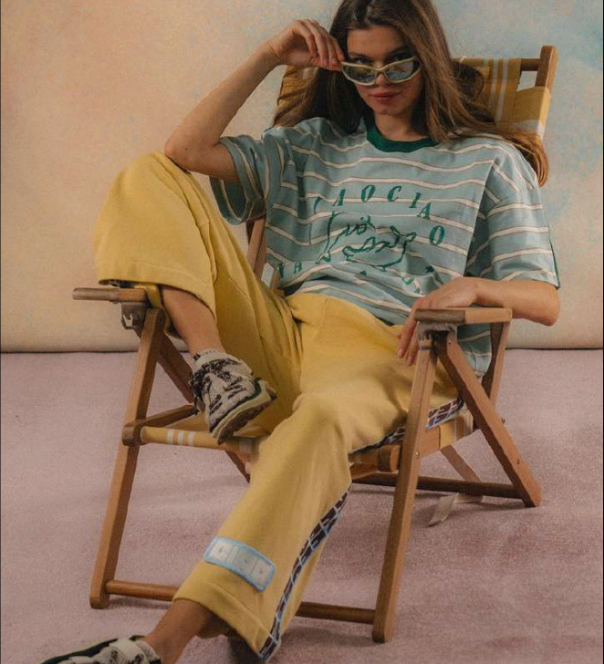Person sitting on a chair wearing a striped shirt and yellow pants in a casual setting.