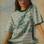 Person wearing a striped t-shirt with text and graphics on a textured wall background